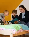 Dans une chambre d'enfants, 2 enfants avec une éducatrice font la lecture. 