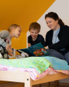 Dans une chambre d'enfants, 2 enfants avec une éducatrice font la lecture. 
